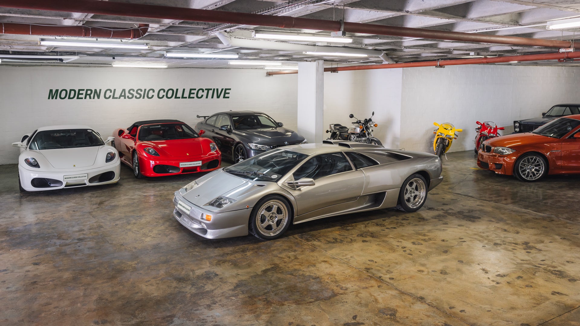 This Modern Classic Collectives showroom, displaying a Lamborghini Diablo SV and a Ferrari F430 Spider F1 and Ferrari F430 Coupe and a BMW 1M in Valencia Orange and two classic ducati 996s and a Honda CBX