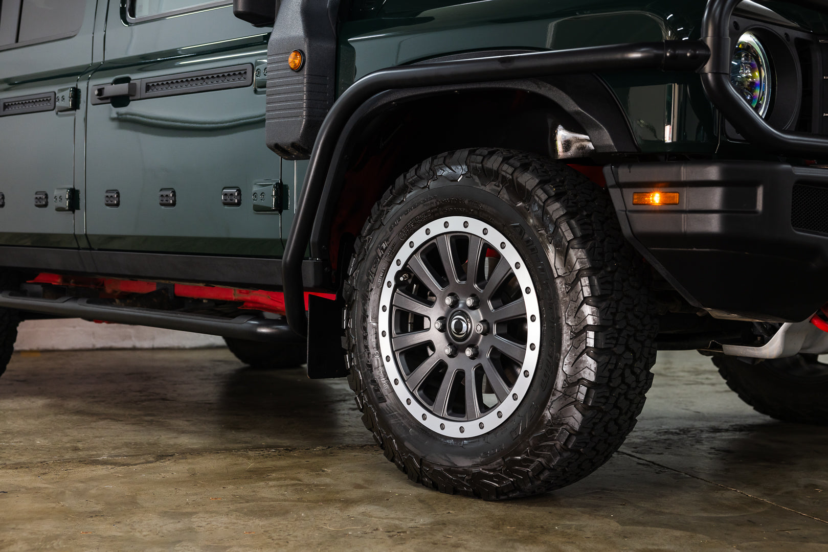 Close-up of a vehicle tire with off-road tread pattern on a concrete floor.